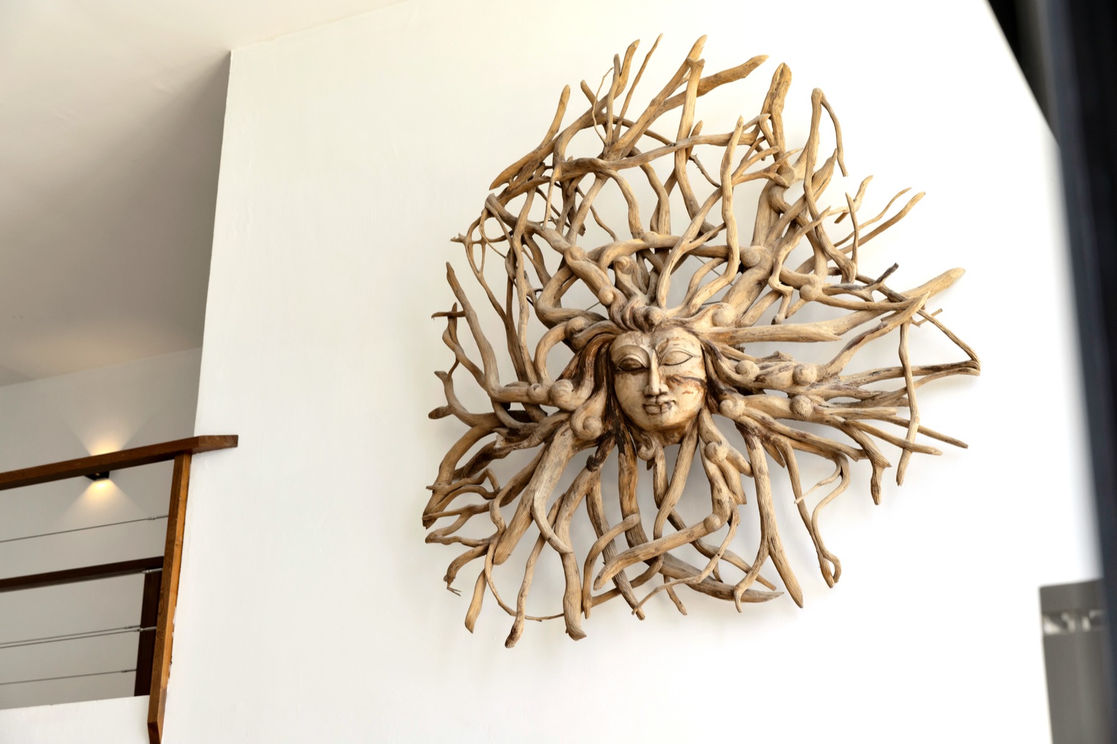 Intricate driftwood sun goddess wall sculpture in a luxury Bonaire villa, highlighting the modern interior design with high ceilings and a wooden staircase.